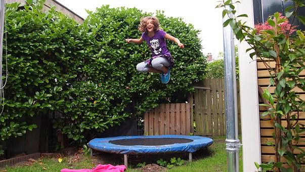 A girl jumps on a trampoline in the yard